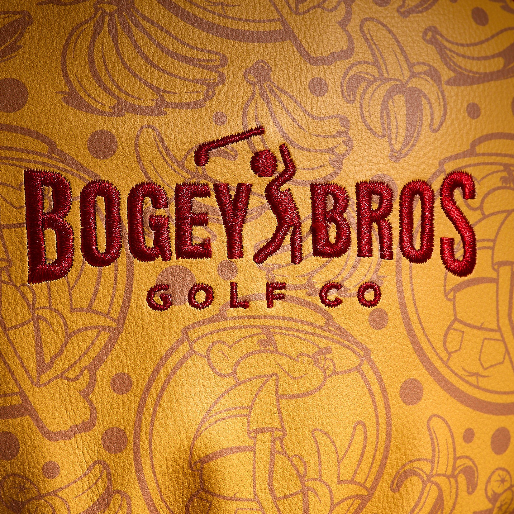Close-up of the Johnny Chimpo - Driver Headcover, crafted from premium PU leather and highlighted by bold red BOGEY BROS GOLF CO embroidery. The background features a lively, repeating pattern of playful line-drawn bananas and cartoon golfers. The detailed texture and precise stitching make this embroidered golf headcover an eye-catching woven label accessory for any golf course.