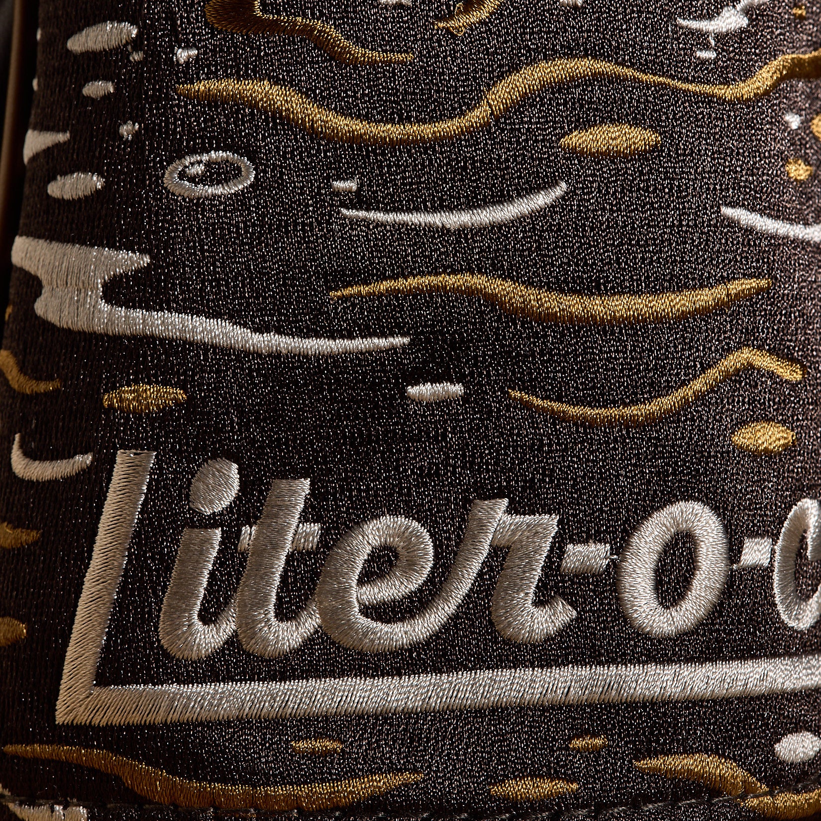 Featuring the Liter-O-Cola name intricately embroidered in white, this premium PU leather driver headcover is adorned with raised, textured stitching and fluid lines and shapes in gold, beige, and white—evoking dynamic splashes or liquid. The complex contrast and exceptional detailing make this Liter-O-Cola - Driver Headcover a true standout on the course.