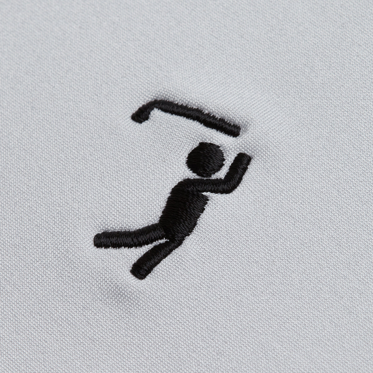 A simple black embroidered stick figure on white fabric appears to hold or swing a curved object above its head, with one leg bent and one arm raised, suggesting movement or action—much like an athlete in motion, this design would pair perfectly with the Bone - Hoodie for both comfort and performance.