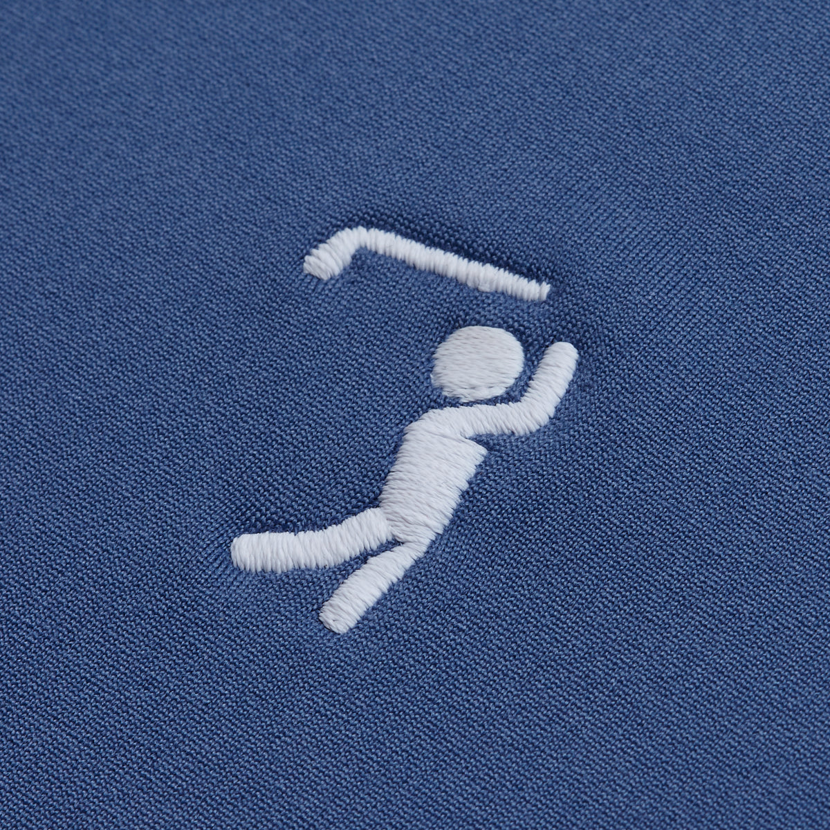 A white embroidered stick figure swings a golf club across the textured blue fabric of the Cooler Blue - Hoodie, perfectly accenting this athletic piece. The figure features a minimalist design with a round head, raised arms gripping the club, and bent legs for a dynamic golf swing effect. Crafted from super stretchy, moisture-wicking material, this hoodie ensures all-day comfort both on and off the course.