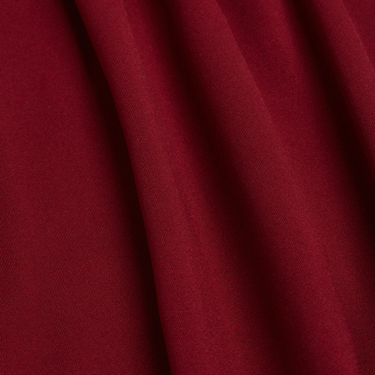 A deep burgundy hue in a smooth, matte fabric with gentle vertical folds and subtle shadows created by its graceful drape; the soft texture suggests an air of luxury and elegance—an ideal choice for apparel such as the Burgundy - Hoodie.