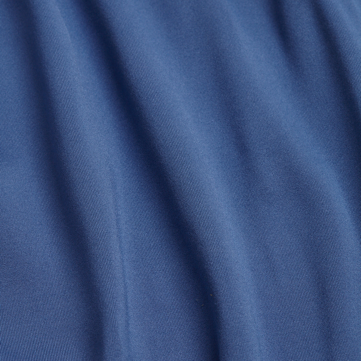 A close-up of soft, blue fabric with gentle vertical folds and a smooth texture. The material appears matte, and the light enhances the natural creases and shadows, highlighting the fabric’s drape—ideal for the Cooler Blue - Hoodie thanks to its super stretchy, moisture-wicking qualities.