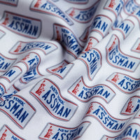 The ASSMAN - Polo features white fabric printed with overlapping New York license plate designs reading “ASSMAN” in blue, red borders and details, and offers UPF 50 protection for sunny days.