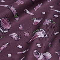 A close-up of maroon Course Candy - Polo fabric shows a whimsical print with tacos, hot sauce, chili peppers, limes, and napkins in pink, green, and white. The athletic fit offers comfort plus moisture wicking for all-day wear.