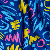 A close-up of the Booyah - Polo shows blue fabric with an abstract pattern of yellow, pink, and light blue squiggles and zigzags. The playful design covers the slightly wrinkled surface and offers UPF 50 protection for sunny days.