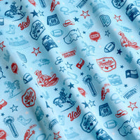 Light blue fabric patterned with red and blue Texas-themed icons: cowboy boots, hats, armadillos, cacti, “Howdy” and “Y’all” text, footballs, stars, the Texas flag, oil derricks, the Alamo, and outlines of Texas. The material shows gentle folds.