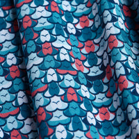 A close-up of Eyes Up Here - The 305 - Polo shows blue, teal, white, and coral abstract floral patterns on textured fabric with an athletic fit, featuring petal-like shapes and thin vertical lines throughout.