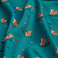The Found A Nut - Polo features teal fabric with orange squirrels holding golf clubs, white golf balls, and red flags. Slightly wrinkled for texture, it offers UPF 50 protection and a playful golfing squirrel design.