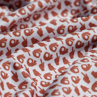 A close-up of the Get In The Hole - Polo shows white fabric with a repeating pattern of small, brown OK hand gesture icons. The athletic fit material features soft folds and shadows that highlight the detailed design.