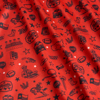 Red fabric with black illustrations: cowboy boots, hats, guitars, Texas state outline, cacti, sheriff badges, stars, speech bubbles with “Y’all,” Texas flags, boots, and Howdy phrases, all scattered and slightly wrinkled.