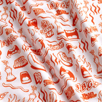 A close-up of the Glizzy Gobbler - Polo’s white fabric, decorated with orange BBQ-themed hot dogs, grilling tools, and playful phrases. Gentle folds highlight its UPF 50 protection—perfect for sunny outdoor gatherings.
