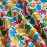A close-up of the Gummy Bears - Polo shows a playful cartoon gummy bear pattern in red, yellow, green, orange, and blue on soft fabric with gentle folds. This cheerful design offers UPF 50 protection for superior sun safety.