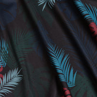 A close-up of Haolie Nights - Polo shows teal, red, and green tropical palm leaves on black fabric. The moisture-wicking material keeps you cool and dry with its soft, gently textured surface.