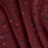Maroon fabric with small white stars and dark Western-themed icons, including cowboy hats, boots, boots, horseshoes, “Y’all” text, a sheriffs badge, guitars, and other rodeo motifs, scattered throughout. The fabric has a slight textured, wavy appearance.