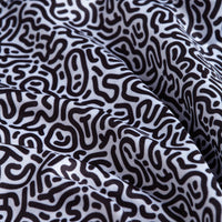Close-up of white, moisture-wicking fabric from the Hidden Words - Polo, featuring wavy folds and an abstract black squiggle pattern resembling maze lines. Soft shadows emphasize the texture and waviness of the material.