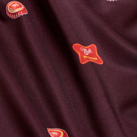 Close-up of Mulli - Polo’s maroon fabric with scattered motifs in red, yellow, and white. A red badge reads Multi and ART VINTAGE in yellow. The fabric has soft folds, a subtle sheen, and UPF 50 protection for style and comfort.