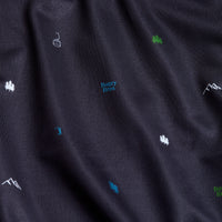 A close-up of the Pine - Polo shows dark, ribbed athletic fabric with subtle folds. Small white and green embroidered mountain, tree, and flag icons decorate it, with 