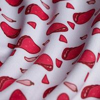 A close-up of the Pink Taco - Polo's white fabric shows a repeating pattern of red steak and chili pepper illustrations. Slightly wrinkled with curved shadows, it features moisture wicking for comfort and playful style.