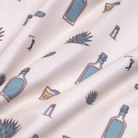 The Reposado - Polo features cream-colored fabric with blue bottles, shot glasses, agave plants, and drinking silhouettes printed on it. Soft folds add texture, while UPF 50 protection ensures stylish sun safety.