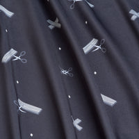 Close-up of the Scissor Me Timbers - Polo, showcasing dark fabric with a subtle sheen, athletic fit, soft folds, and gentle draping. Features small white scissors cutting paper strips and tiny diamond motifs for stylish comfort.