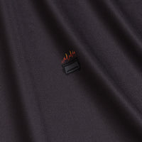The Scorched - Polo features dark, ribbed, moisture-wicking fabric with a subtle sheen and soft folds. A small embroidered rectangular toaster with orange and red flames sits slightly left of center on the chest.