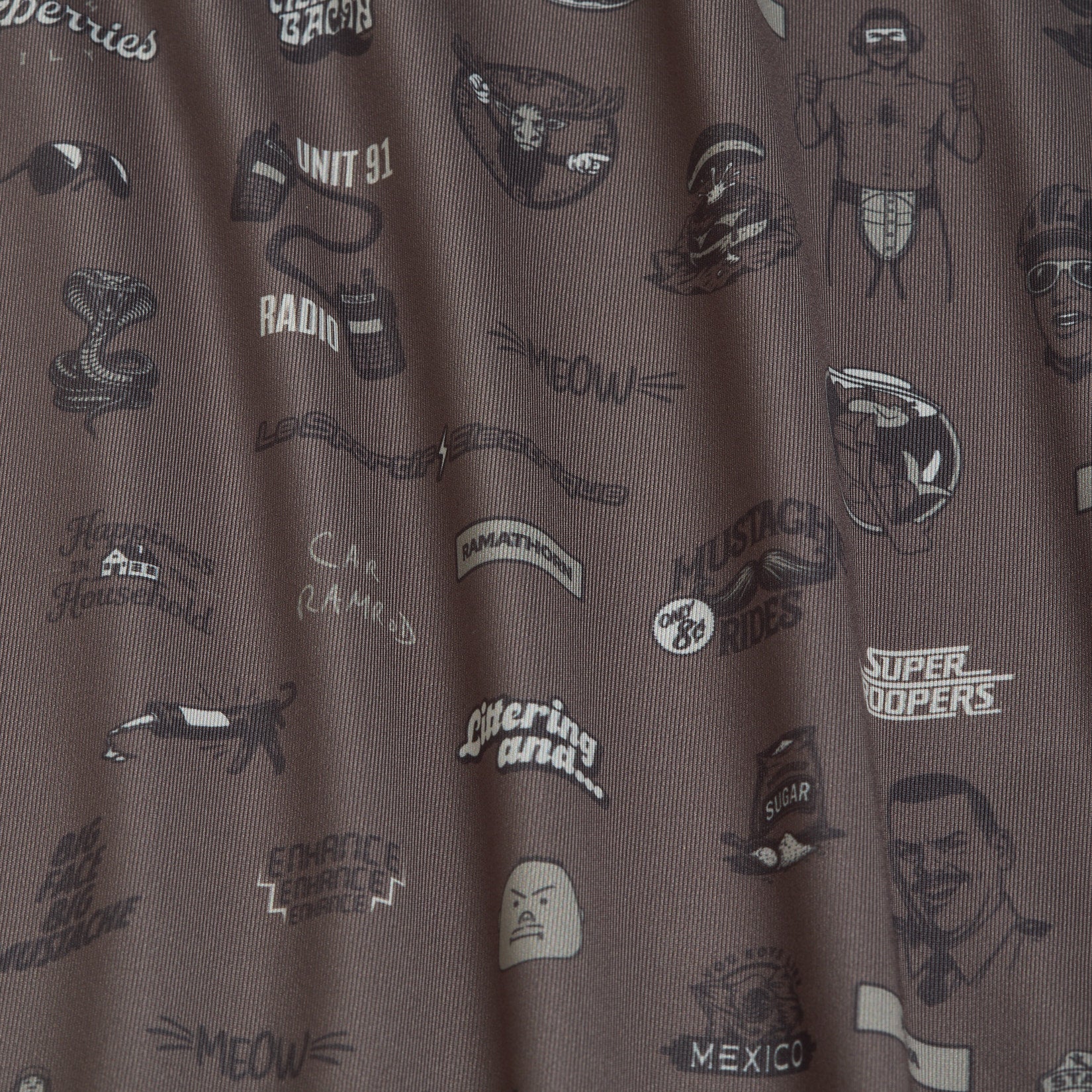 Brown fabric with black outlined illustrations including a football helmet, a muscled man, a radio, sunglasses, a snake, a raccoon, text phrases like Meow, Littering and…, Super Troopers, and other doodles from the movie Super Troopers..
