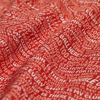 A close-up of the Swing Thoughts - Polo’s red, moisture-wicking fabric, featuring overlapping white text in varied fonts and sizes. The athletic fit material displays a textured, wavy pattern for a bold, dynamic look.