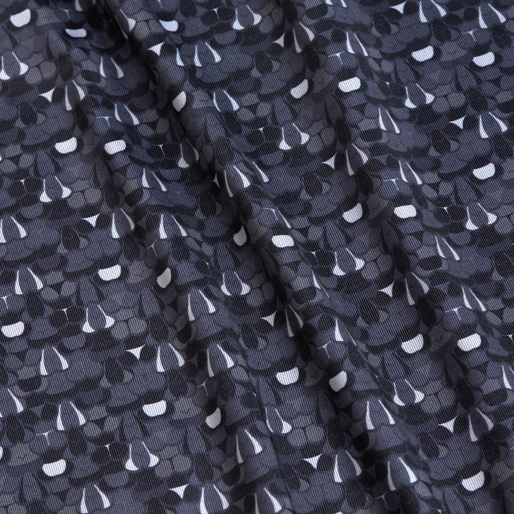 Close-up of the T&A - Fitty Shades - Polo, featuring rippled black fabric with a repeating abstract pattern in white, grey, and black. This athletic fit polo offers dynamic style and moisture wicking comfort.