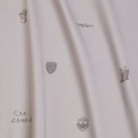 White fabric with small, sparse black line illustrations: two soda cups, three police badge shapes, the word MEOW, and the text CAR RAMROD, all randomly placed. The fabric shows subtle vertical folds and shadows throughout.