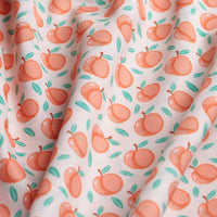 The Tooty Frooty - Polo features a playful orange peach and green leaf pattern on white fabric, with gentle folds and shadows. Its slightly wrinkled material offers moisture-wicking comfort in a vibrant fruit motif.