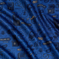 Ringling Road - Polo features gently rippled blue fabric adorned with playful black outlined illustrations, including guitars, cowboy hats, microphones, arcade machines, stars, a bearded man, and “Ringling Rd” street signs. The textured surface adds dimension and subtle shadows to the lively pattern.
