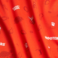 The Wingin' It - Orange - Polo features bright orange fabric with playful prints—fried chicken drumsticks, golf balls, a Hooters uniform, soda cup, BOGEY BROS text—and offers an athletic fit with moisture-wicking comfort for all-day wear.