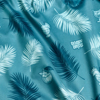 The Boat Drinks - Women's Polo features a teal fabric with tropical palm leaves in white and dark blue, playful illustrated cocktails and coconuts, an athletic fit for comfort, and subtle repeating Bocel Bros. text that blends into the summery print.