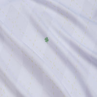 A close-up of the Dublin Down Women's Polo shows soft white fabric with a diamond pattern, faint yellow dashed lines, and a green four-leaf clover motif at the center. The material is moisture-wicking for extra comfort.