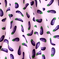 A close-up of the Eggplant - Women's Polo shows light pink, moisture-wicking fabric with a playful print of small purple eggplants with green caps. The slightly wrinkled material features gentle folds and shadow details.