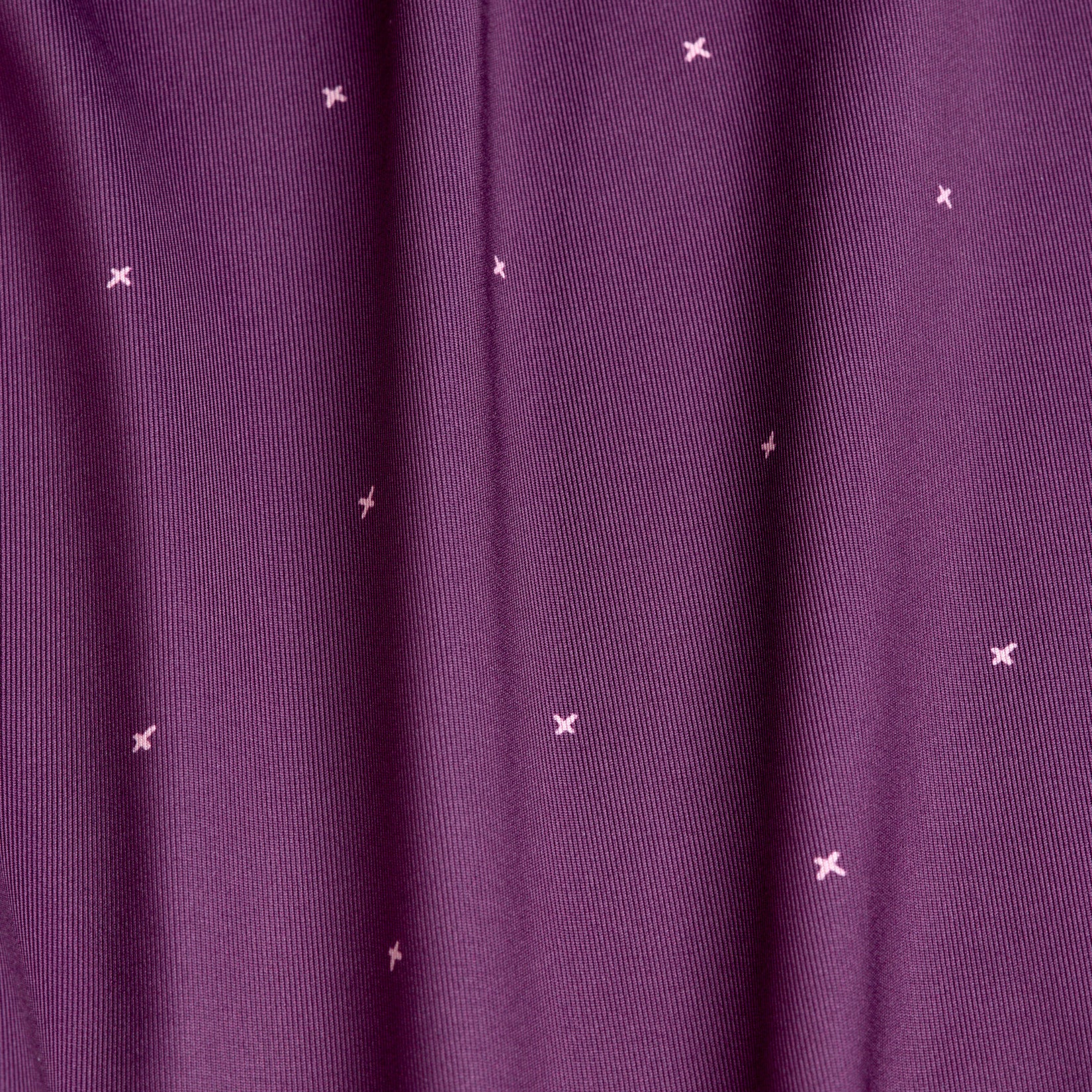 A close-up of Exes - Plum - Women's Polo fabric features small light pink embroidered x shapes, soft vertical folds, and a smooth texture with moisture-wicking properties for added comfort.