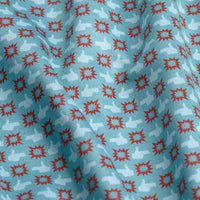 A close-up of the Finger Bang - Women's Polo fabric: blue with red geometric starburst patterns and light blue abstract shapes, featuring visible folds, subtle texture, and UPF 50 protection that creates varied shadows and highlights.