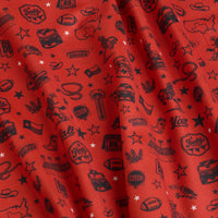 Red fabric printed with small black illustrations and text, including cowboy hats, Texas shapes, boots, footballs, stars, “Howdy,” “Y’all,” “Everything’s Bigger,” and other Western-themed motifs. The fabric has visible folds and shadows.