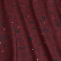 Close-up of maroon fabric with small black sketches of cowboy hats, boots, and bandanas, mixed with white stars and Yall! text. The surface is slightly wrinkled, making the designs appear at varying angles and depths.
