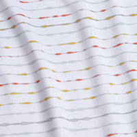 A close-up of the Heat Index - Women's Polo shows white, moisture-wicking fabric with wavy gray, yellow, and orange lines. Soft and lightly textured, gentle folds create shadows; the lines are slightly irregular and dotted.