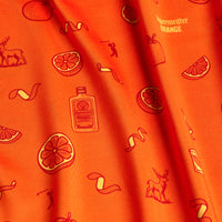 The Main Squeeze - Women's Polo features orange fabric with sliced oranges, peel spirals, an “ORANGE” bottle, deer, and dancing figures. Its athletic fit offers comfort and style with a Jägermeister Orange logo in the top right corner.