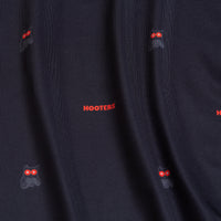 Close-up of Night Owl - Women's Polo: dark fabric with small red-eyed owl faces and bold red “HOOTERS” text, evenly spaced. Features athletic fit, fine ribbed texture, subtle folds, and moisture-wicking properties.