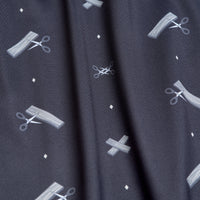 A close-up of the Scissor Me Timbers - Women's Polo shows dark, moisture-wicking fabric with white scissors, cut lines, Xs, and diamonds in a whimsical pattern; athletic fit fabric displays texture and a slight vertical fold.