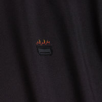 Close-up of Scorched - Women's Polo in dark, pinstriped, moisture-wicking fabric. A small embroidered bucket with three red and yellow flames warns against washing with hot water or exposing to fire.