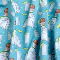 The Tequila - Women's Polo features blue fabric with illustrated tequila bottles, salt shakers, lime wedges, and shot glasses in a repeating pattern. Moisture-wicking material has subtle wrinkles for soft shadowed texture.
