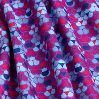 A close-up of Whale Tail - Women's Polo fabric shows a vibrant abstract pattern in red, pink, purple, and blue with gentle folds and shadows. The slightly wrinkled fabric also offers moisture wicking for comfort.