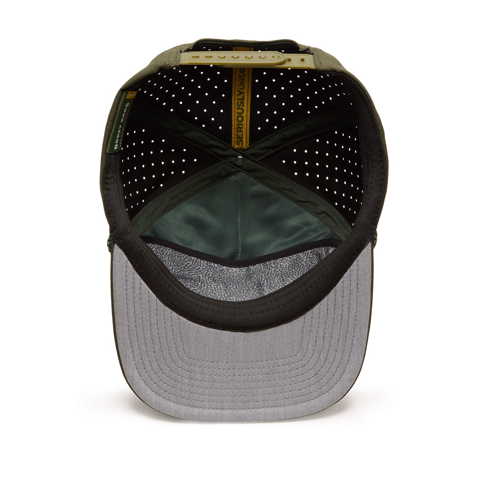 The image shows the inside of a green baseball cap with a gray underside of the brim, perforated black lining, and a yellow band labeled SERIOUSLY FUN. The adjustable strap and stitching details are visible. The cap rests on a white background.