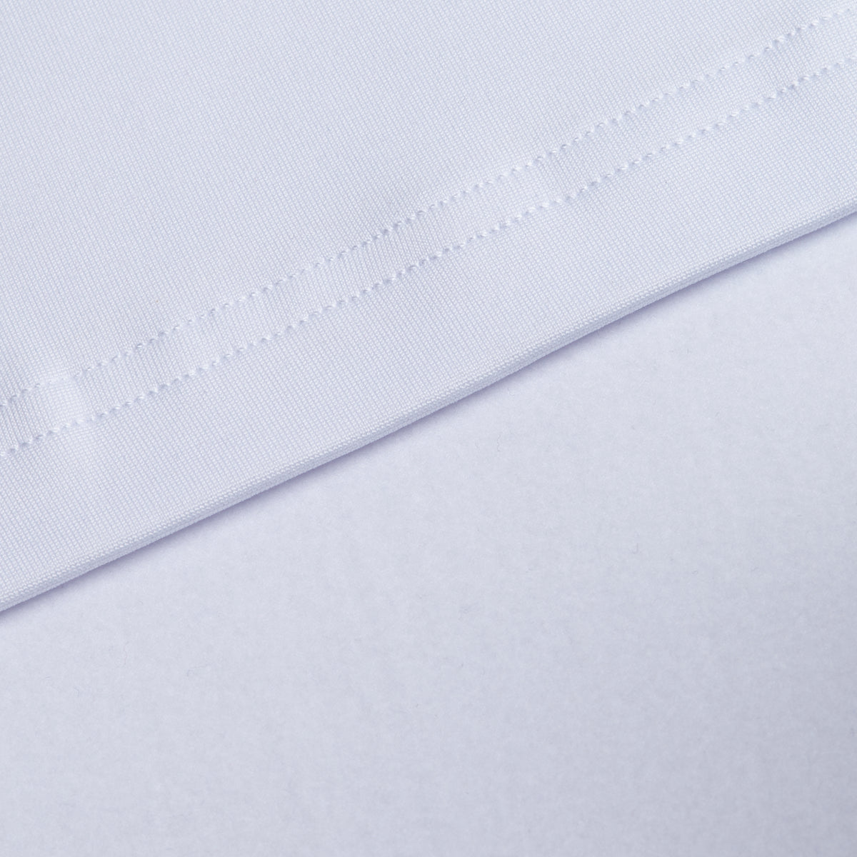 Close-up of two layers of smooth white fabric from the White - Hoodie. The top layer features a stitched hem with visible threads forming a diagonal line. Engineered for performance, this material provides moisture wicking properties to keep you dry and comfortable. The bottom layer is flat and unhemmed, offering a soft, textured background. Even, bright lighting highlights the details.