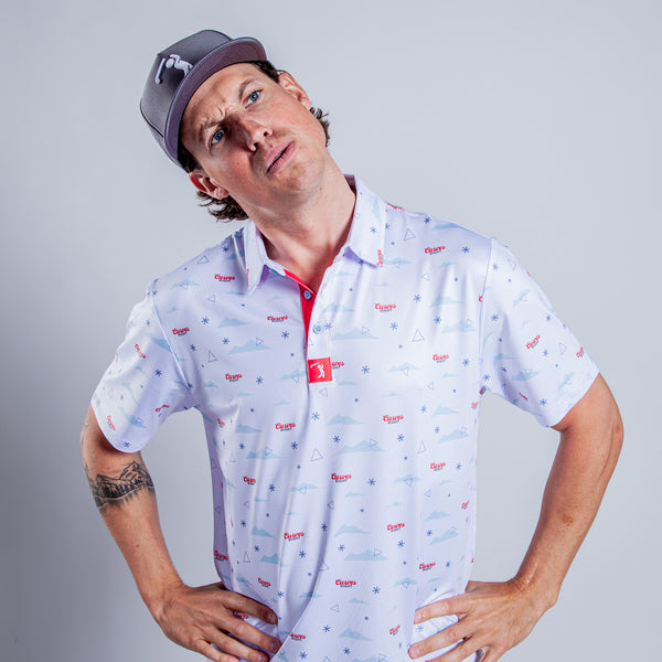 Wearing the Curves Right - Polo, a person in a gray cap stands with hands on hips, head tilted and eyebrow raised in a quizzical expression. A small tattoo appears on their left forearm against a plain, light background.