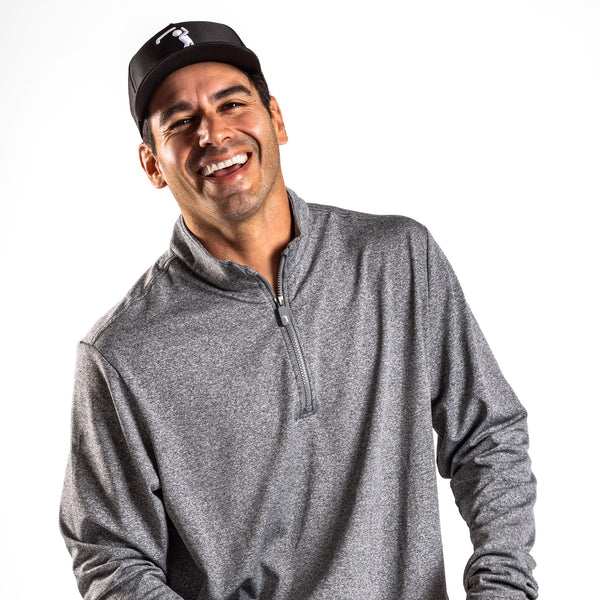 A smiling man with dark hair is wearing the Heather Gray - Q-Zip, a heather-gray quarter-zip pullover with an athletic fit, along with a black baseball cap featuring a white golf logo. Against a solid white background, he laughs energetically, his head tilted slightly to his right.